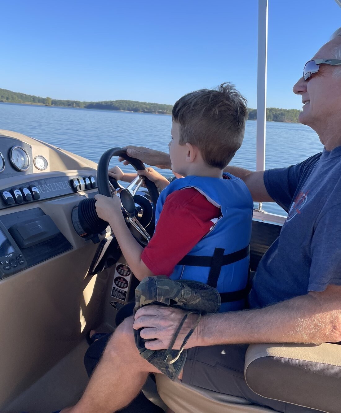 Todd laughing beside a small boy at the wheel of a boat